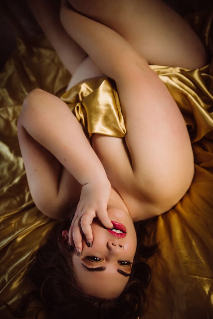a confident bare elegance guest poses on golden satin sheets in a boudoir photo