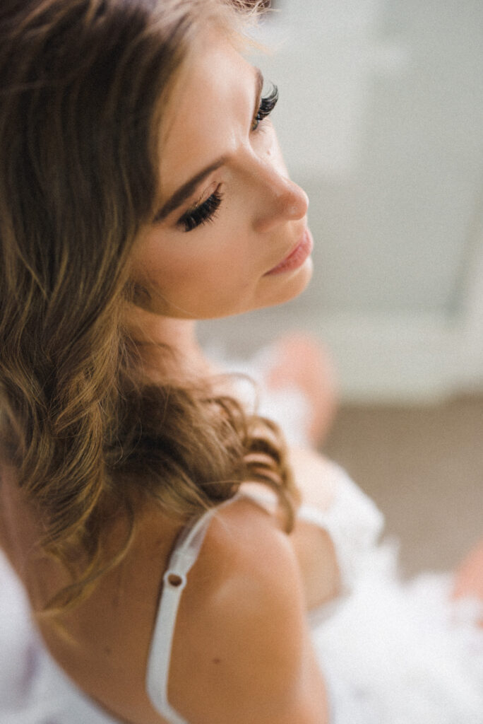 a woman in a white robe looks over her shoulder in a luxury boudoir photoshoot