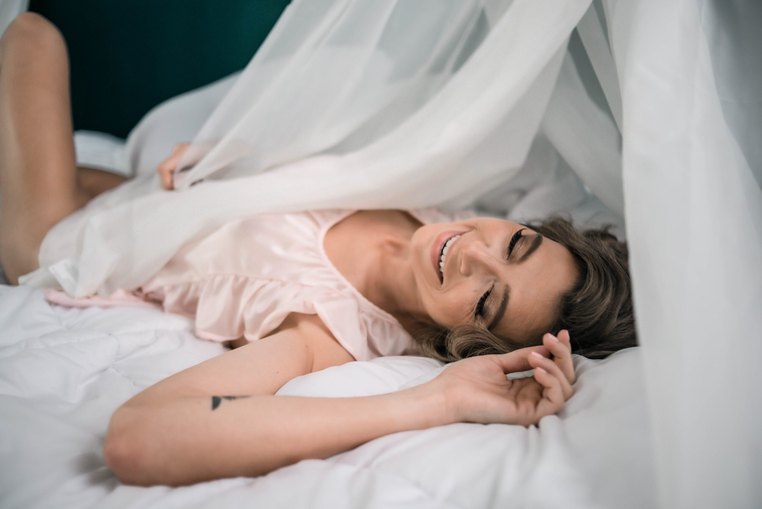 a smiling woman laying on a white canopy bed with natural styling