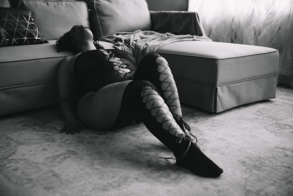 a woman sitting on the floor in lingerie leans back onto a couch