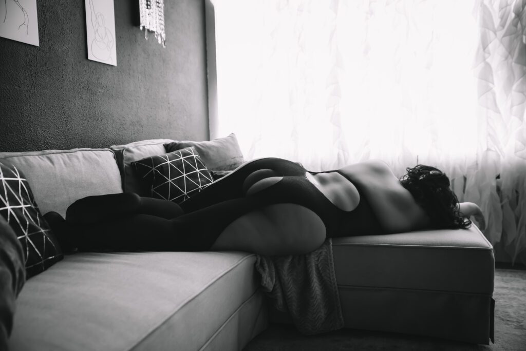 a black and white image of a woman laying on a couch in lingerie