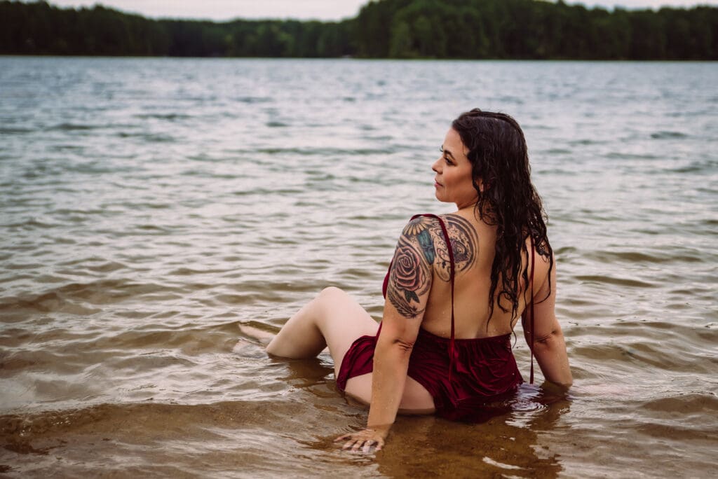 a woman poses on a lakeshore showing off her tattoos