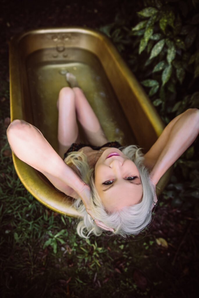 a woman leaning back in a gold tub outdoors gazes into the camera