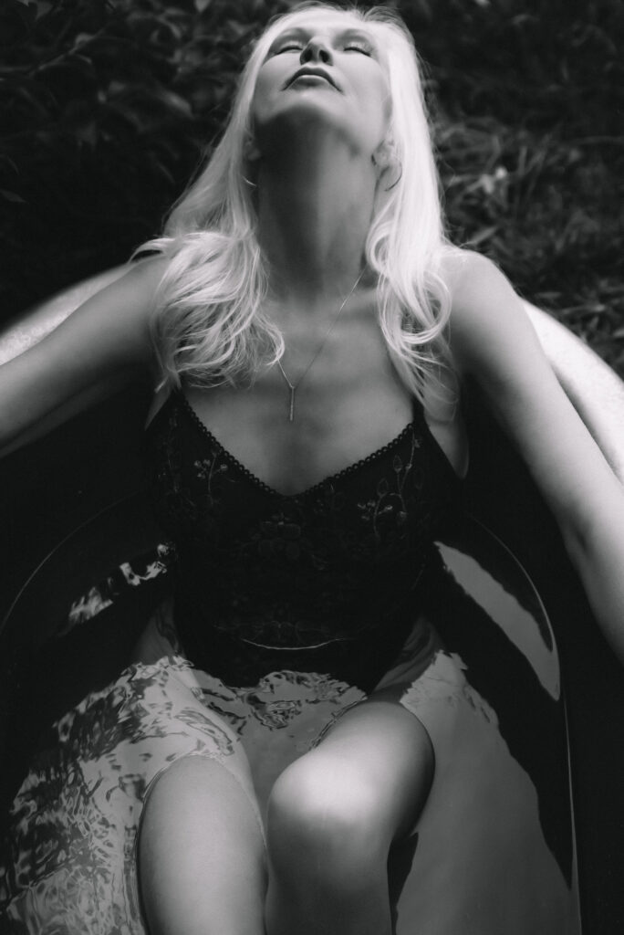 a black and white boudoir image of a woman wearing lingerie leaning back in a bathtub