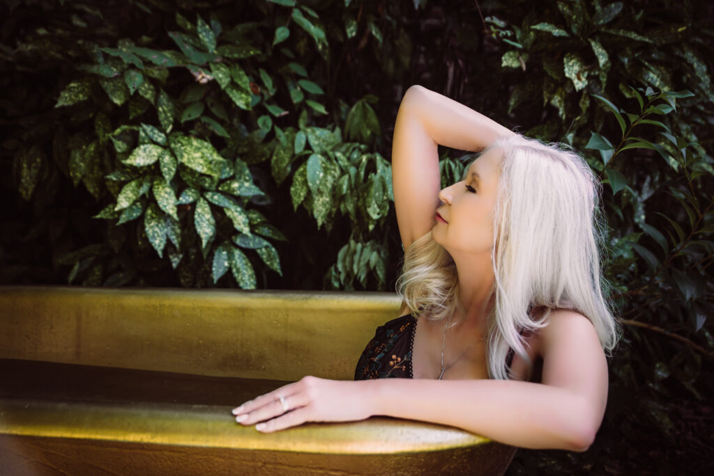a confident woman poses in a golden tub looking to the left side of the frame with her hand in her hair