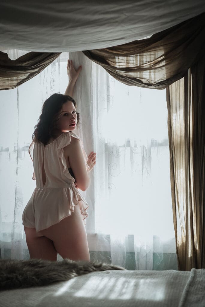 a woman poses in draped fabric in front of an illuminated window