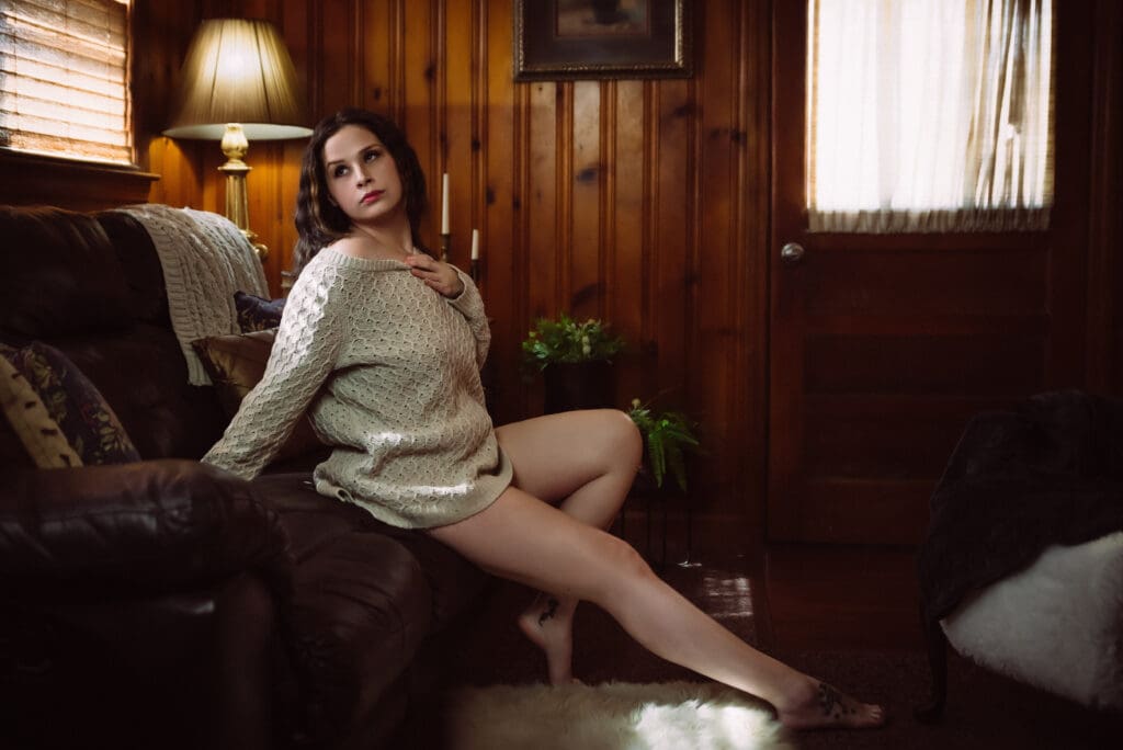 a woman poses in a wood paneled room wearing a sweater in golden light