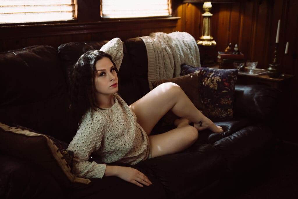 a woman poses on a leather couch in a boudoir photoshoot
