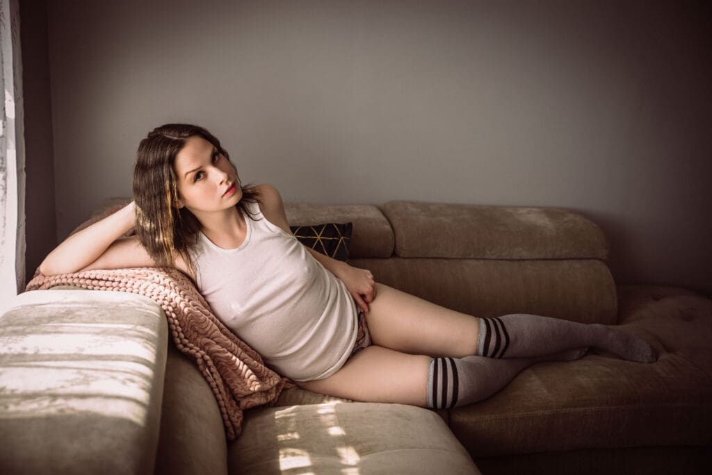 a woman posing in a white tank top and high socks on a couch