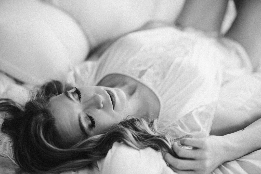 a black and white image of a woman laying on a bed touching her hair