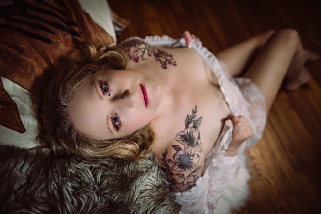 a woman poses showing off her tattoos in a boudoir photoshoot with bare elegance boudoir