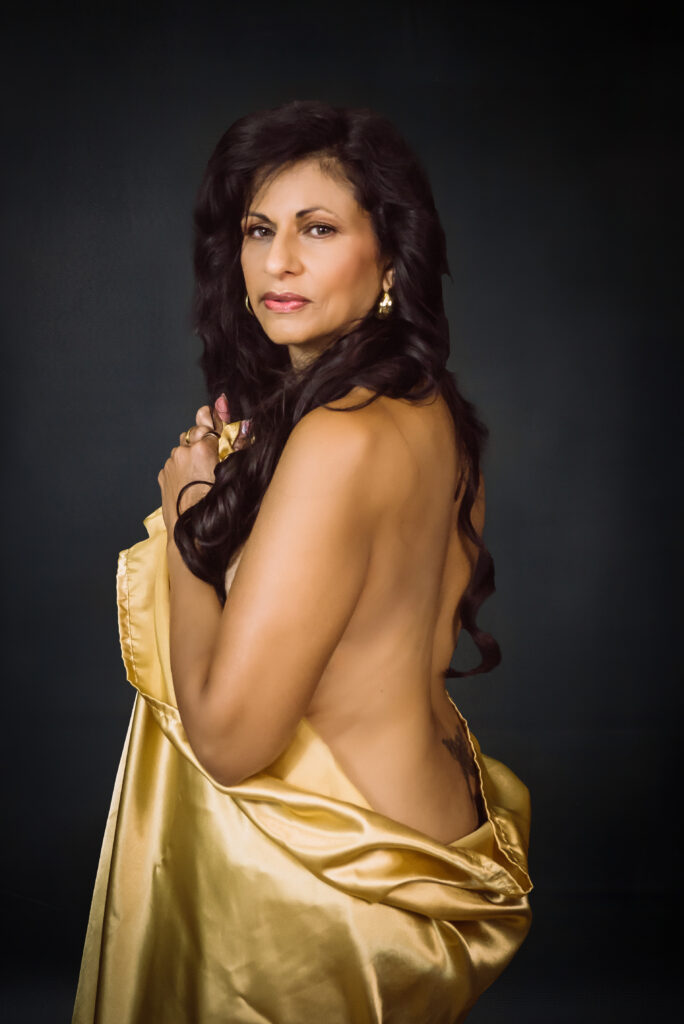 A woman poses for a boudoir portrait with a gold satin sheet looking over her shoulder